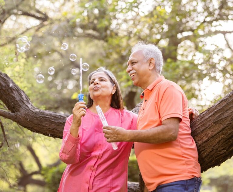 Senior couple sharing a joyful, playful moment while blowing bubbles outdoors.