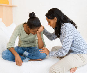 A Woman comforting a distressed teenage girl while sitting together on a bed