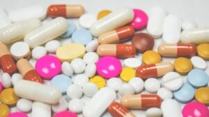 A variety of pills and tablets in different shapes and colors scattered across a wooden table surface.