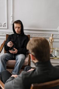 A man in a hoodie sits in a chair next to another man