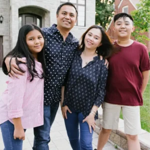 A family smiles together for a photo in front of their house