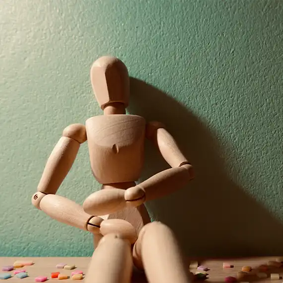 Wooden figure holding its stomach amidst scattered pills, representing physical discomfort or medication management.