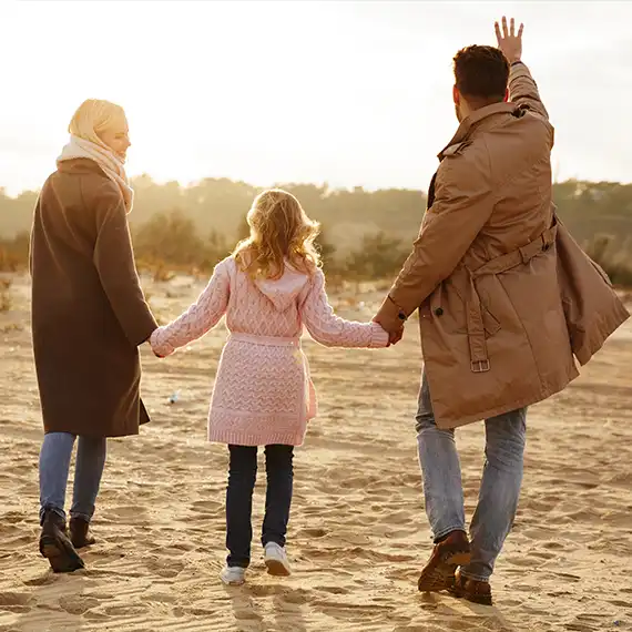 Family walking hand-in-hand on the beach at sunset, symbolizing unity and a hopeful future together.