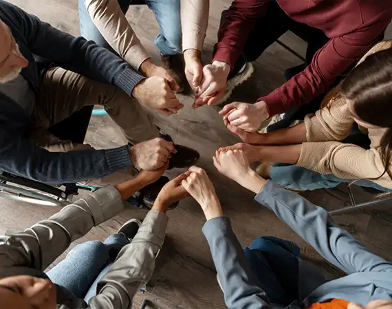 Diverse group holding hands in a circle during a supportive group therapy session.