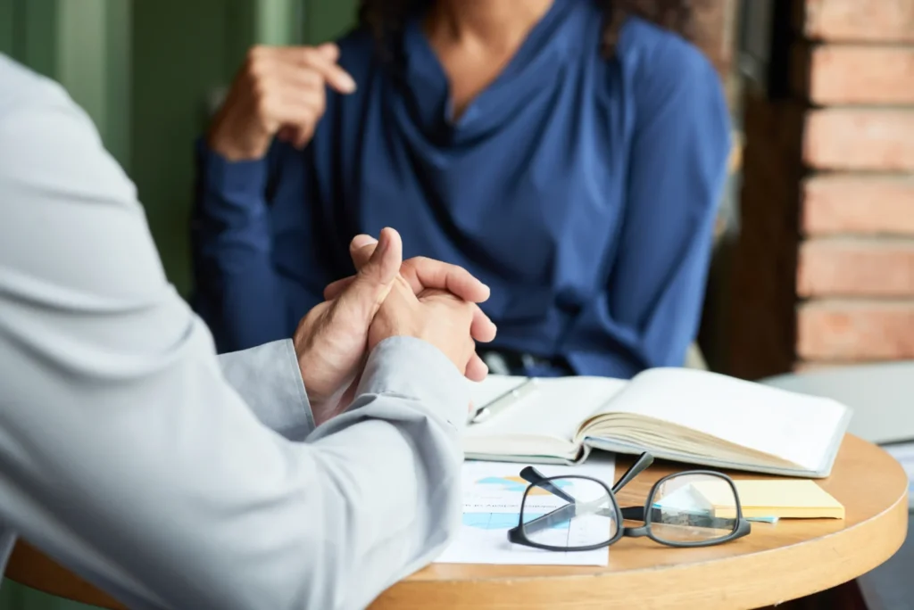 Therapist with clasped hands listening attentively to a client during a professional consultation session.