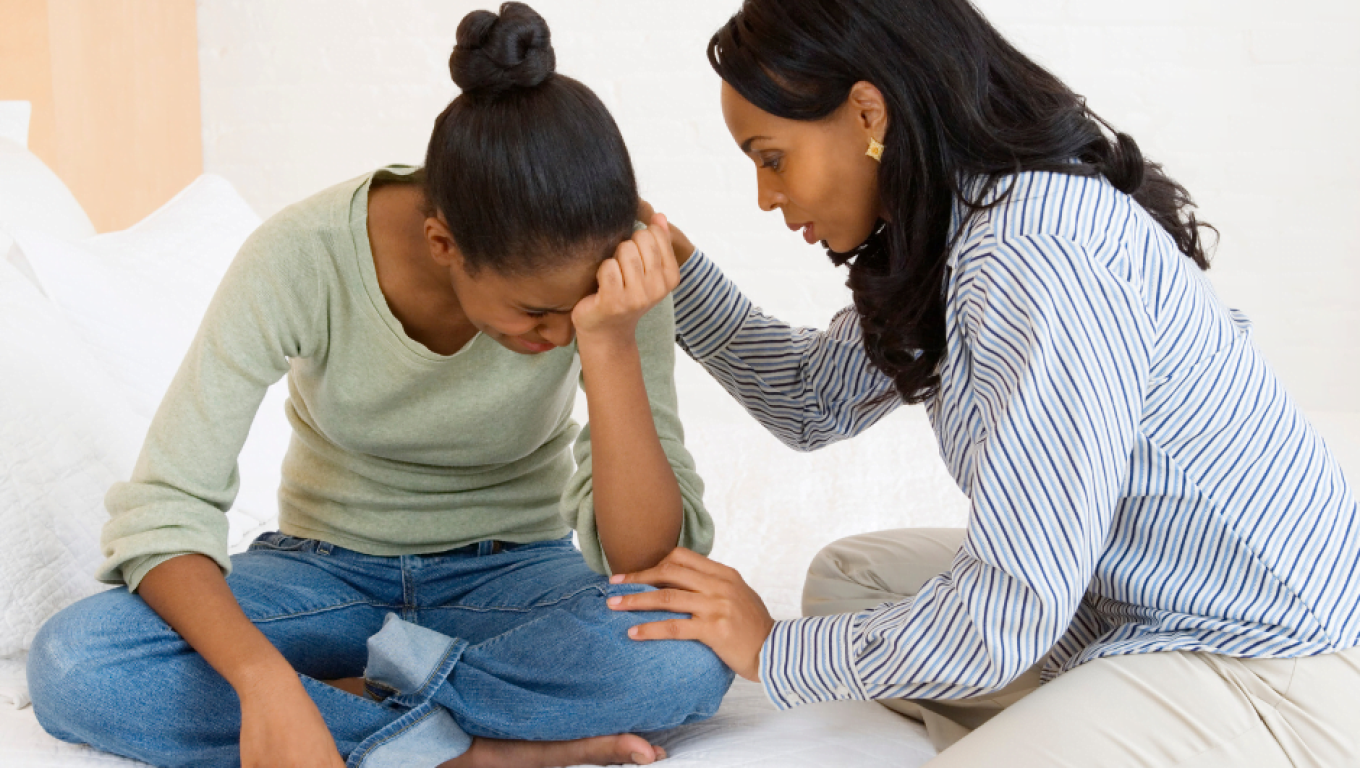 A Woman comforting a distressed teenage girl while sitting together on a bed