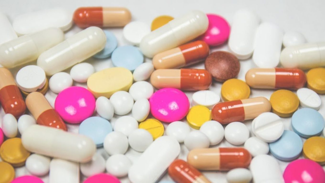 A variety of pills and tablets in different shapes and colors scattered across a wooden table surface.
