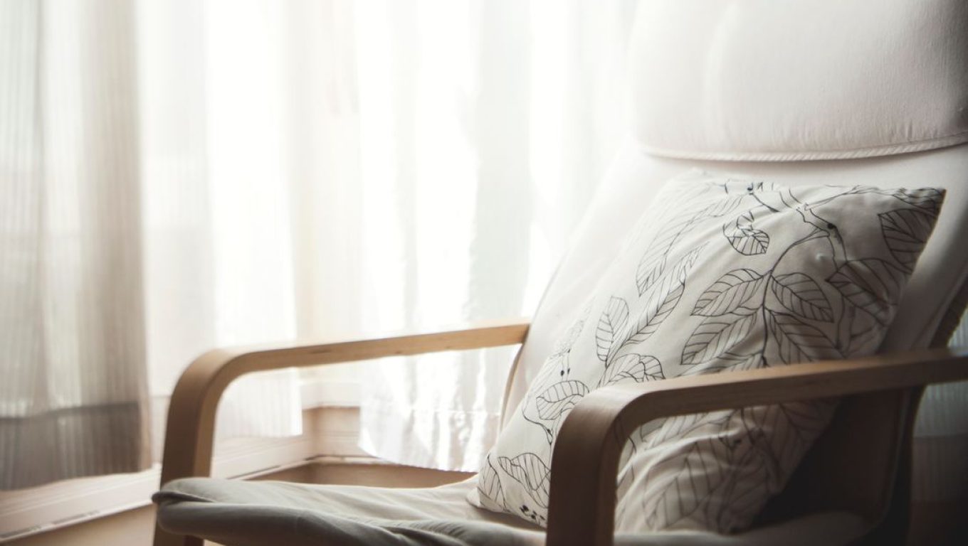 A cozy chair with a decorative pillow beside a bright window