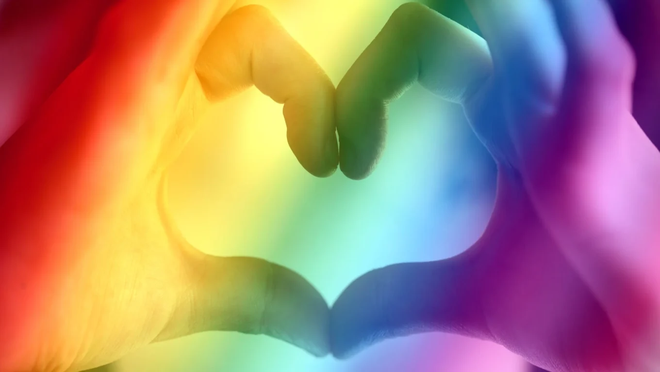 Two hands forming a heart shape against a rainbow-colored background