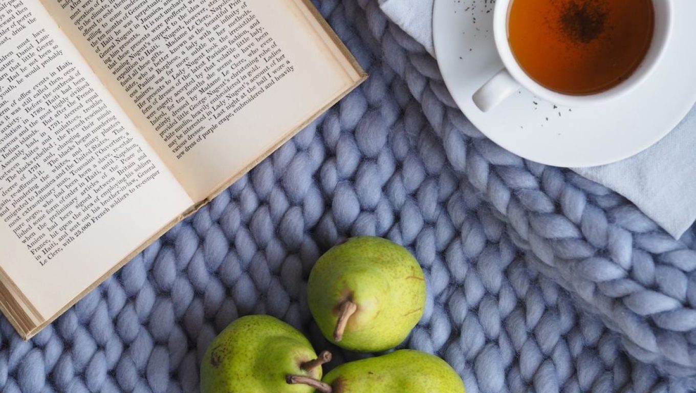 A cup of tea and two fresh pears placed on a blue blanket