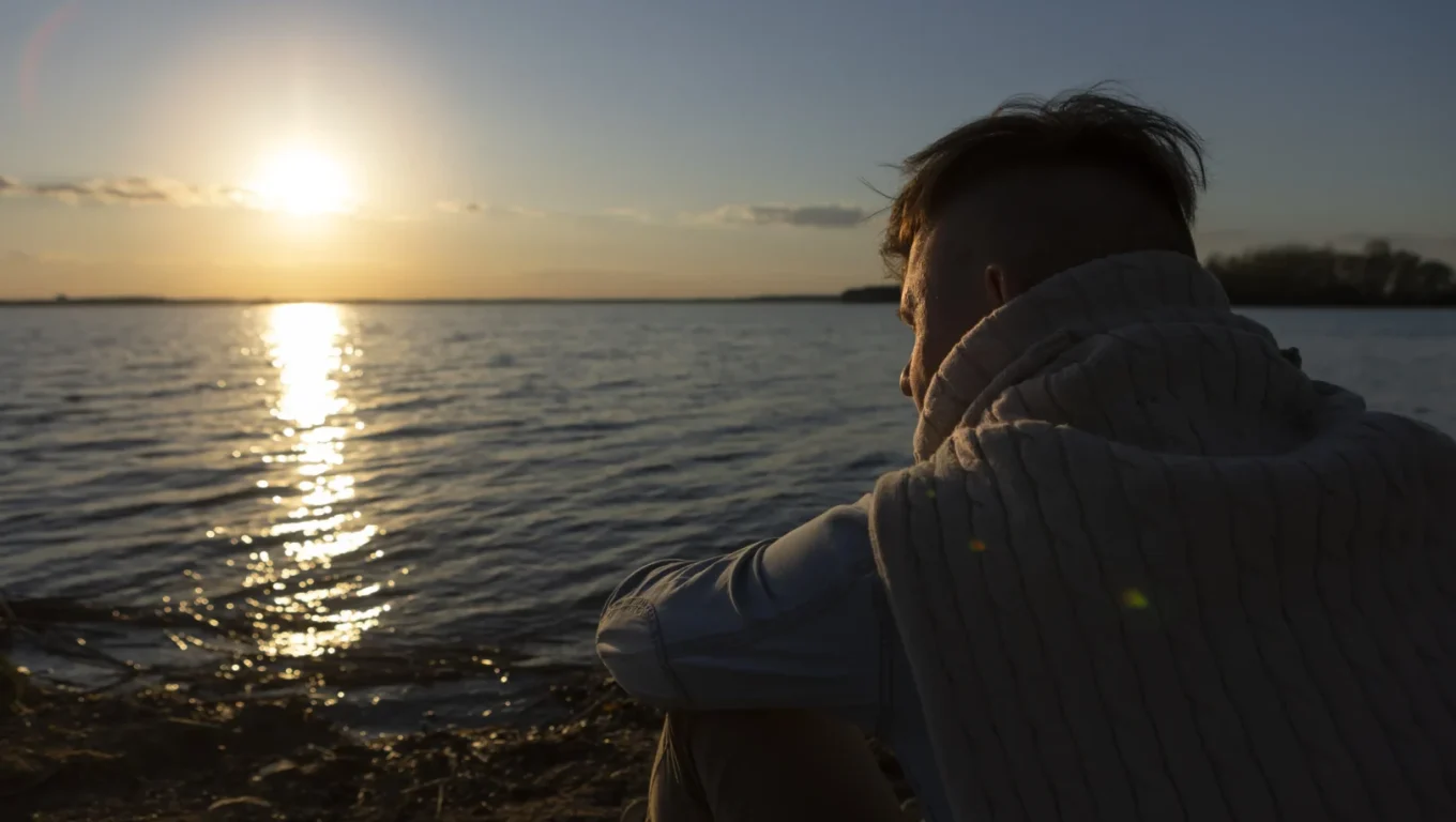A man sitting by a calm lake at sunset, reflecting on techniques for how to be less emotionally reactive.